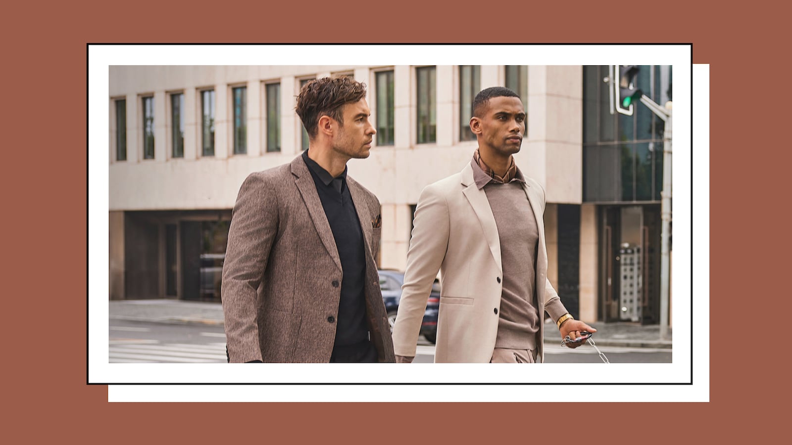 Two Stylish Men in Neutral-Toned Suits Walking Confidently Through an Urban Setting, One in a Brown Textured Suit and Black Shirt, the Other in a Beige Suit with a Sweater and Collared Shirt