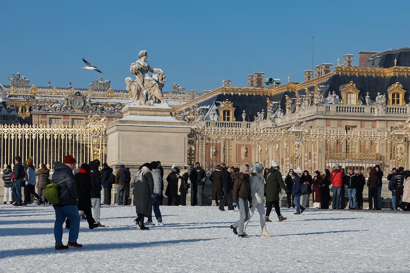 Visitors walk in the snow in front of the "Grille d'Honneur" golden gates of the Chateau de Versailles, in Versailles outside Paris on January 6, 2026. Some of the winter's coldest weather so far hit travel in Britain, France and the Netherlands on January 5, closing roads, grounding flights and forcing train cancellations, including on Eurostar, just days after a power outage caused major disruption. (Photo by GEOFFROY VAN DER HASSELT / AFP via Getty Images)