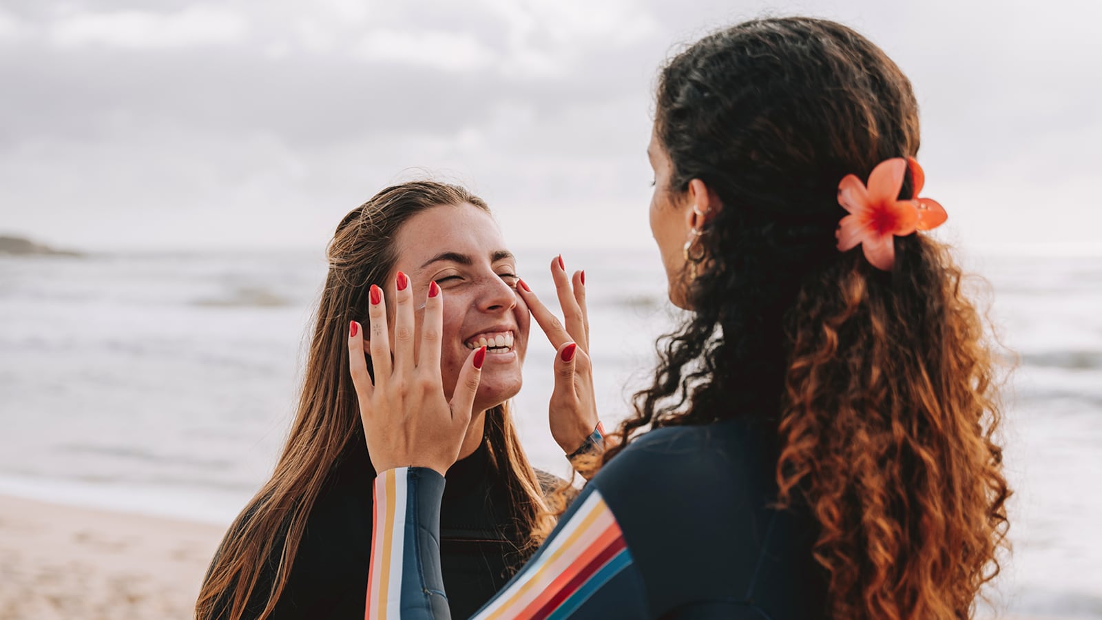 A smiling woman on a beach having sunscreen applied on her face