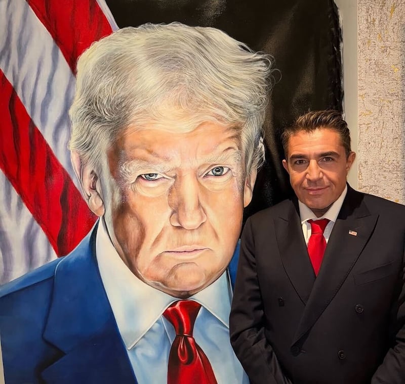 Paolo Zampolli posing in front of a portrait of Donald Trump.
