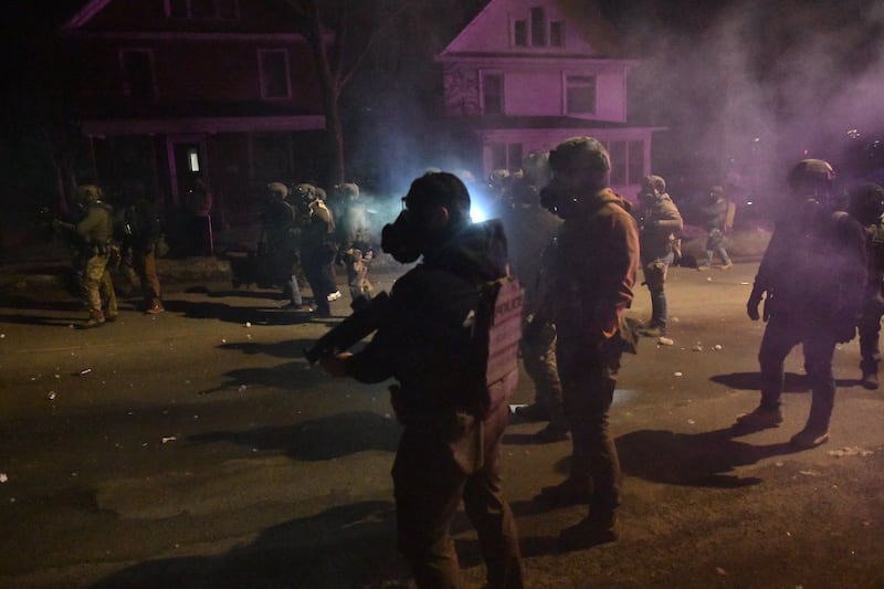 Federal agents and police in riot gear walk amid smoke from crowd-control devices after protests broke out following the shooting of a Venezuelan man by an ICE agent in Minneapolis on January 14, 2026.