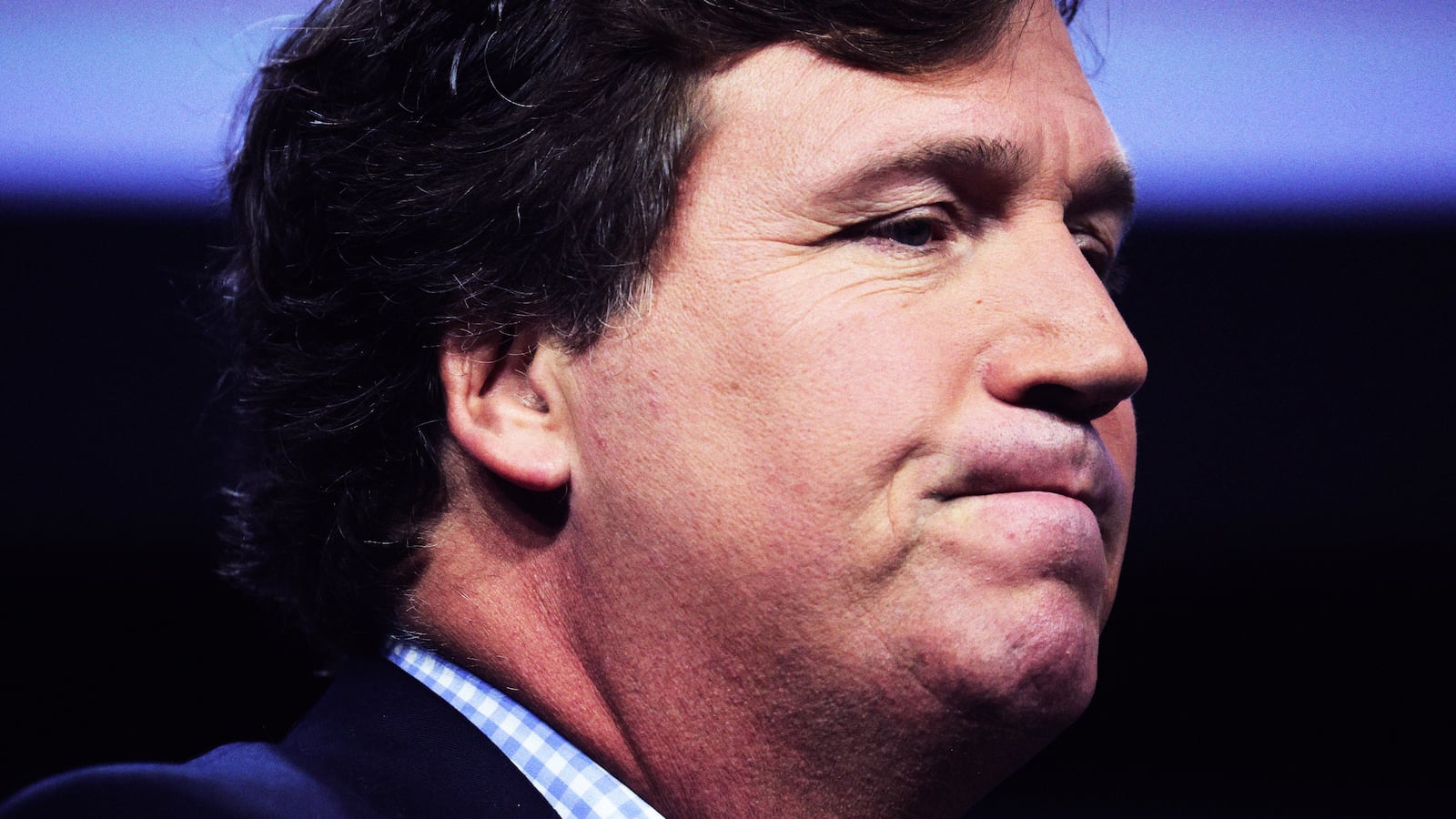 A close up photograph of Tucker Carlson grimacing.