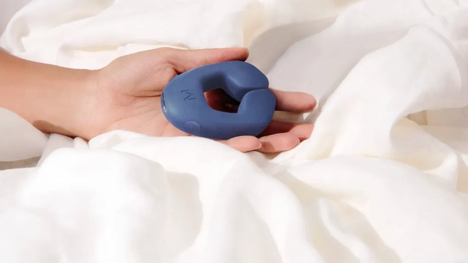 A person holding MysteryVibe's Tenuto Mini Vibrator on a bed with white bed sheets.