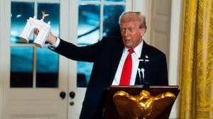 President Donald Trump holds up a model of an arch while delivering remarks during a ballroom fundraising dinner in the East Room of the White House on Wednesday October 15, 2025.