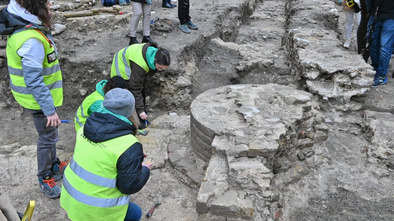Researchers in green neon jackets stand in front of Basilica ruins.