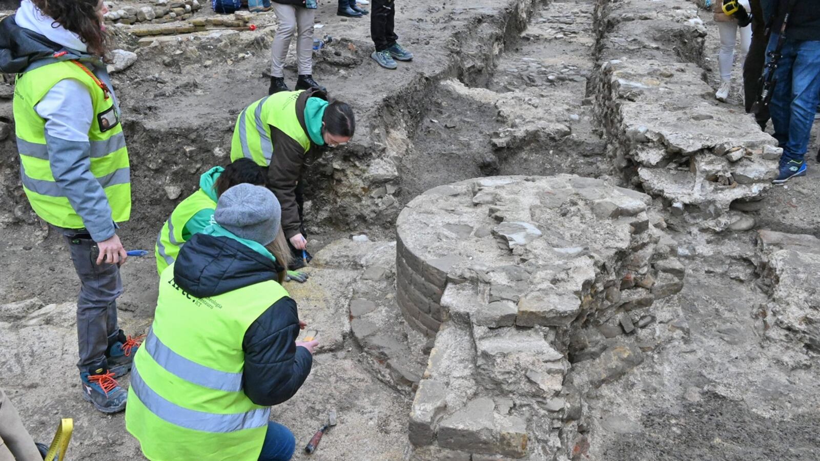 Researchers in green neon jackets stand in front of Basilica ruins.