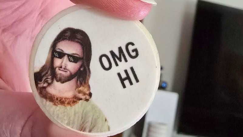 Close up of a hand holding a MAMMAMIA infused communion wafer. It depicts Jesus wearing sunglasses and the text "OMG HI"