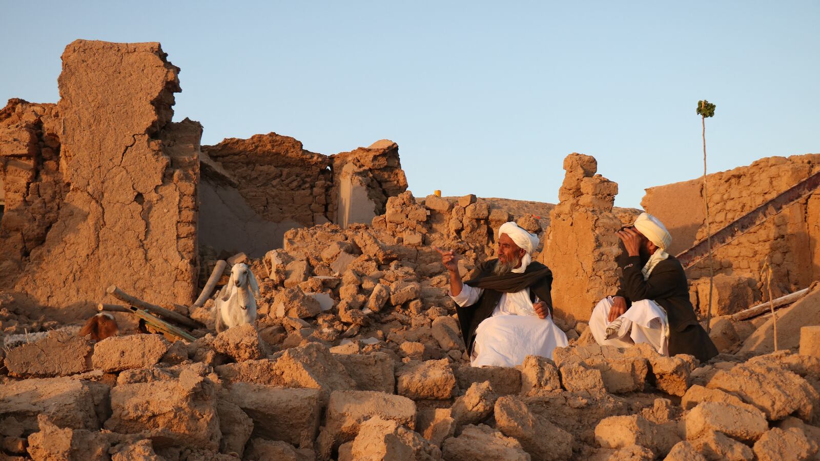 Afghan residents sit at a damaged house after earthquake in Sarbuland village of Zendeh Jan.