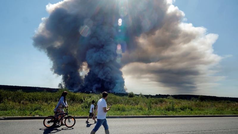 TOPSHOT - Local residents walk past the smoke of a fire at the Russian e-commerce firm Wildberries' logistics complexes in the town of Elektrostal outside Moscow on July 18, 2026. A Ukrainian drone attack on two logistics centres in Russia killed eight people and injured 24, officials said on July 18, 2026, when the Moscow region reported a new wave of drone strikes. Russian e-commerce firm Wildberries said its logistics complexes in Kotovsk and Elektrostal, in the Tambov and Moscow regions respectively, came under attack. One person was killed and 37 were injured at the Elektrostal warehouse, according to the region's governor, Andrei Vorobyov. (Photo by TATYANA MAKEYEVA / AFP via Getty Images)