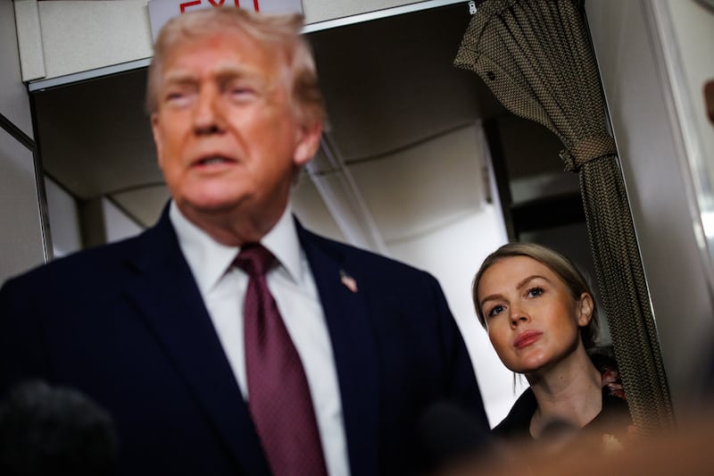 White House Press Secretary Karoline Leavitt listens as U.S. President Donald Trump takes questions from the members of the press aboard Air Force One on January 11, 2026.