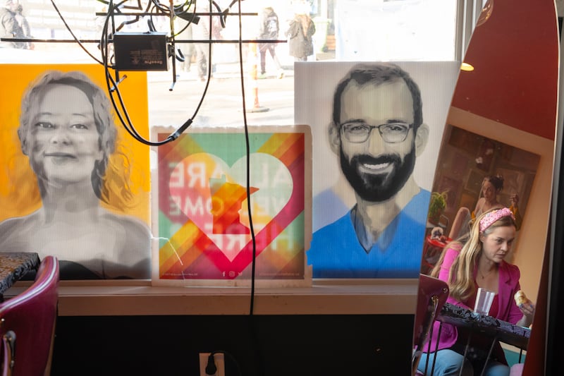 A woman enjoys coffee and doughnuts with her daughter near photos of Renee Good and Alex Pretti
