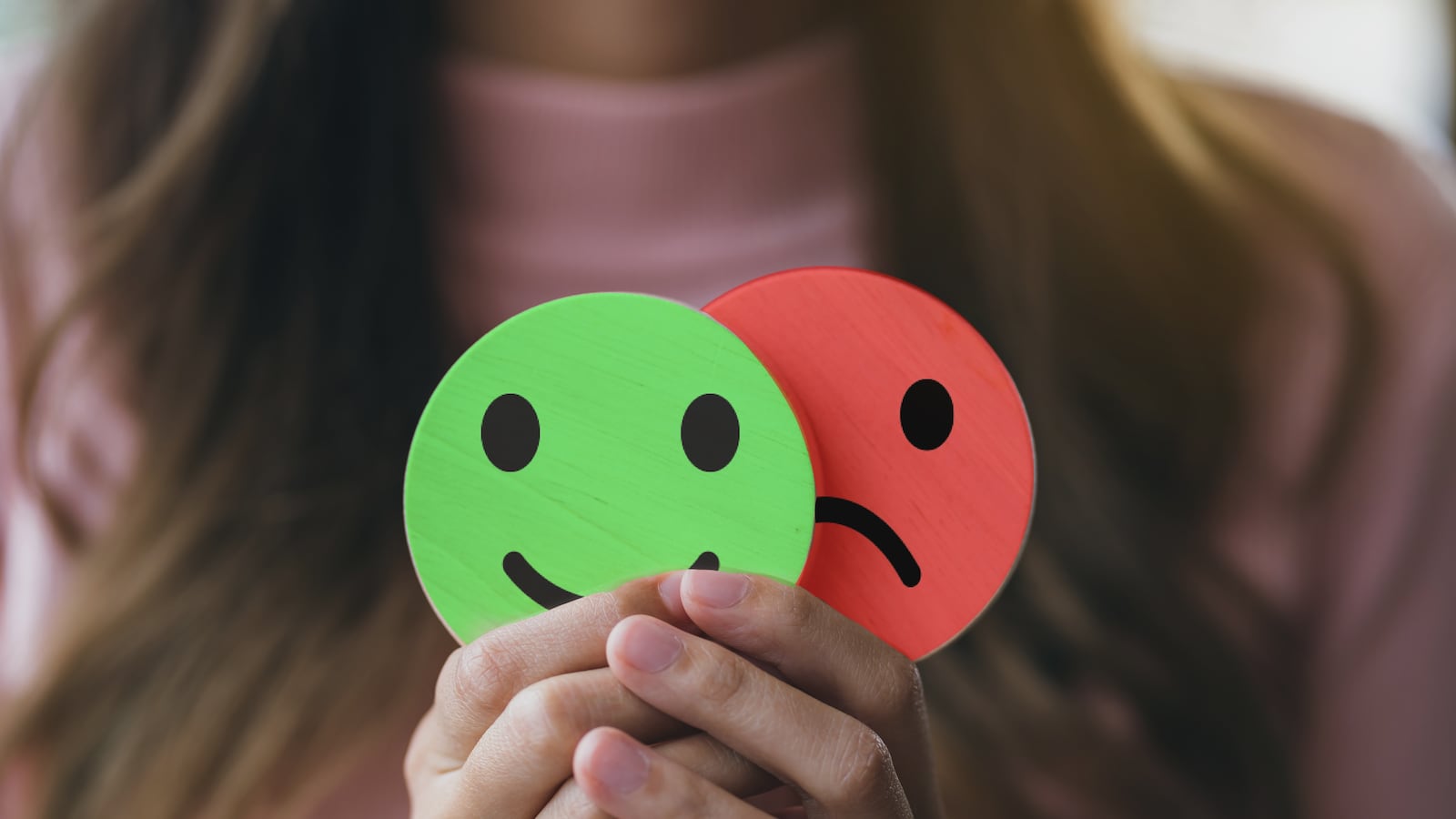 Woman holds signs depicting smiley and sad faces.