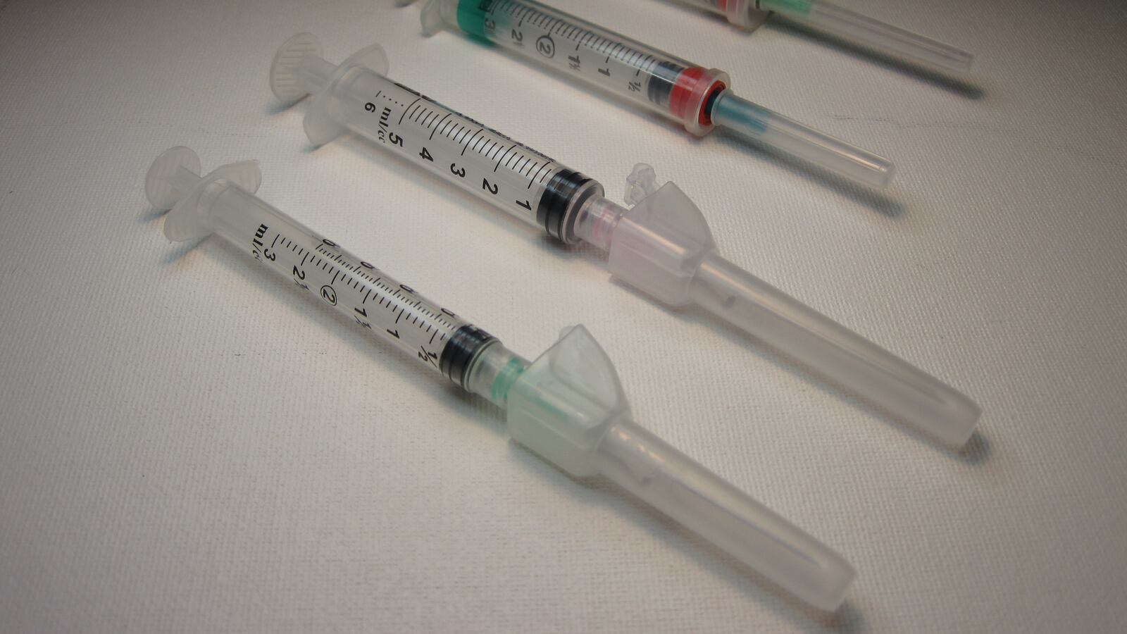 Several syringes of varied volumes and design, with hypodermic needles attached.