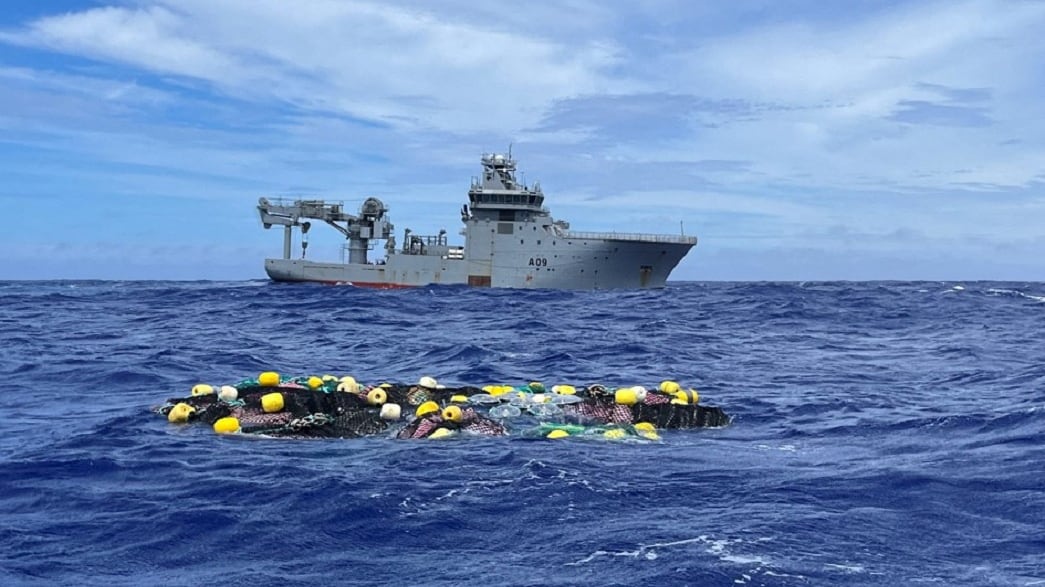 Bags of cocaine float in the Pacific Ocean as a boat floats in the background.