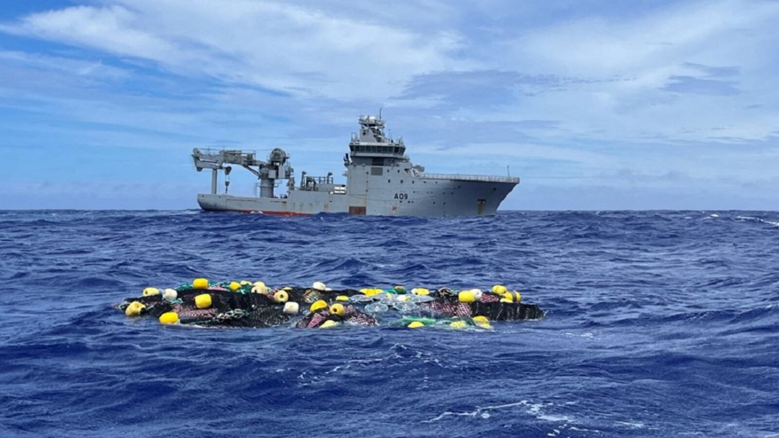 Bags of cocaine float in the Pacific Ocean as a boat floats in the background.