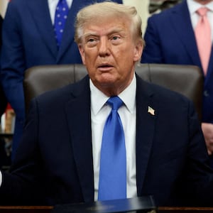 President Donald Trump speaks during a meeting in the Oval Office. He is surrounded by men in suits.