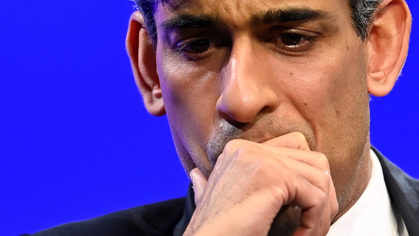 Rishi Sunak puts his hand to his mouth on stage at an event.
