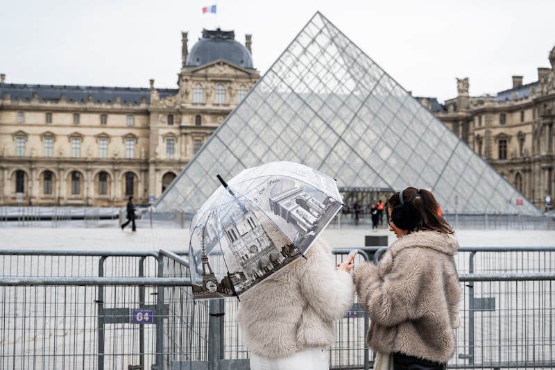 Tourists stand next to barriers blocking the plaza with the Louvre Pyramid, designed by Chinese-US architect Ieoh Ming Pei, as the Louvre Museum is closed due a strike in Paris on January 12, 2026. The Louvre museum was forced to close on January 12, 2026 after its staff, who have been on strike since mid-December in a bid to secure better working conditions, decided to continue their action, AFP learned from the museum and trade unions. (Photo by Martin LELIEVRE / AFP via Getty Images) / RESTRICTED TO EDITORIAL USE - MANDATORY MENTION OF THE ARTIST UPON PUBLICATION - TO ILLUSTRATE THE EVENT AS SPECIFIED IN THE CAPTION