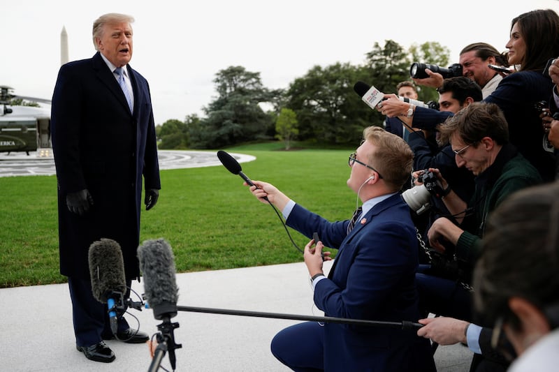 A reporter for Real America's Voice (right) holds out her microphone toward Trump upon his return to the White House.