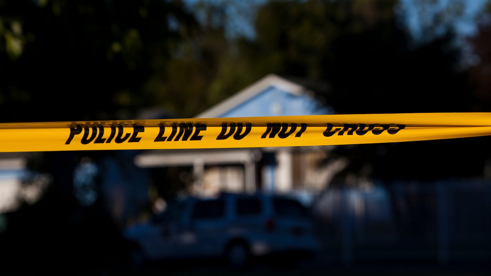 A blue home sits behind yellow police tape.