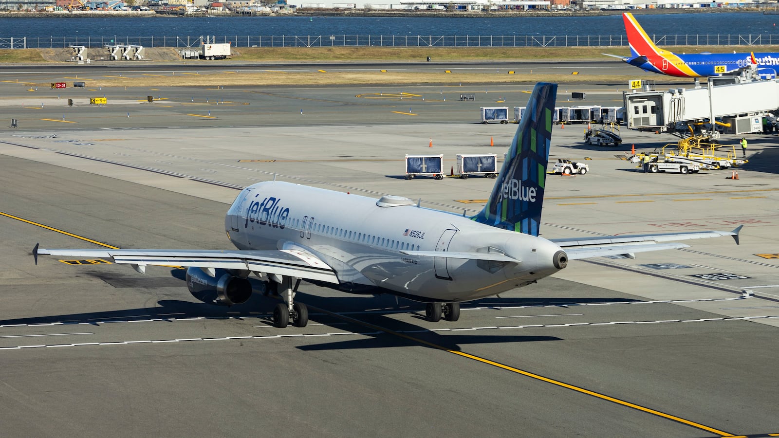 JetBlue Airbus A320-200 passenger aircraft spotted taxiing in LaGuardia airport LGA in New York City while a Southwest Boeing 737 is taxiing in the background. The A320 airplane has the registration tail number N526JL, the name Blues Jsut Want to Have Fun and is powered by 2x IAE jet engines. Jet Blue Airways Corporation is a major airline in the United States with headquarters in Long Island City, Queens, NYC operating domestic and international network routes with a fleet of 286 planes. New York, USA on November 12, 2024