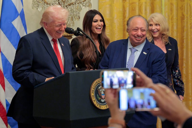 WASHINGTON, DC - MARCH 26: U.S. President Donald Trump reacts on stage with (L-R) U.S. Ambassador to Greece Kimberly Guilfoyle, President and CEO of the Gristedes John Catsimatidis and  his wife Margo Catsimatidis during a Greek Independence Day Celebration at the White House on March 26, 2026 in Washington, DC. President Trump issued a proclamation declaring March 25, 2026 as "Greek Independence Day: A National Day of Celebration of Greek and American Democracy". (Photo by Chip Somodevilla/Getty Images)