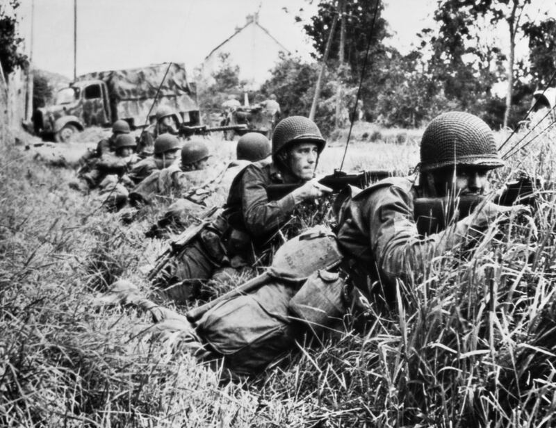 American troops, pressing closely on the heels of retreating Germans in the Battle of Normandy, take cover in a ditch at St. Sauveur-le-Vicomte as they return the enemy fire with rifles and machine guns.