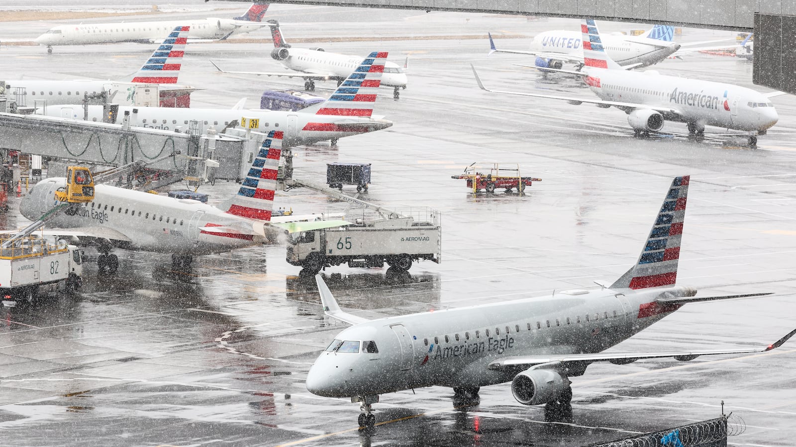 A ground crew de-ices an Embraer ERJ-175 American Eagle passenger plane (L) at LaGuardia Airport in New York on February 22, 2026. A fast-developing storm is threatening to pummel the US East Coast with a foot or more of snow beginning Sunday, bringing Mother Nature's wrath to a region that only just dug out from a previous winter wallop. Meteorologists issued blizzard warnings for New York and parts of at least six states, warning Saturday that heavy snow and gale-force winds are forecast to slam all major cities along the densely populated Interstate 95 northeast corridor, including Philadelphia, Boston and even Washington further south. (Photo by CHARLY TRIBALLEAU / AFP via Getty Images)