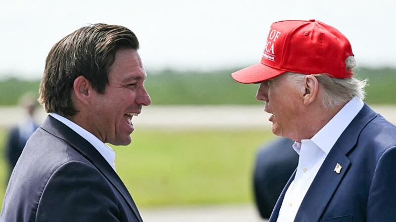 (L/R) Florida Governor Ron DeSantis shakes hands with US President Donald Trump upon Trump's arrival at Dade-Collier Training and Transition Airport in Ochopee, Florida, on July 1, 2025. President Trump is visiting a migrant detention center in a reptile-infested Florida swamp dubbed "Alligator Alcatraz." Trump will attend the opening of the 5,000-bed facility -- located at an abandoned airfield in the Everglades wetlands -- part of his expansion of deportations of undocumented migrants, his spokeswoman said. (Photo by ANDREW CABALLERO-REYNOLDS / AFP) (Photo by ANDREW CABALLERO-REYNOLDS/AFP via Getty Images)