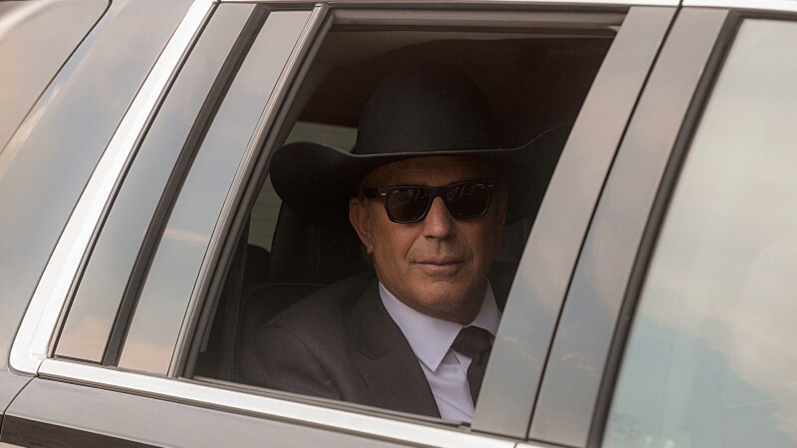 Kevin Costner wears sunglasses and a cowboy hat in a car with a rolled down window in a still from "Yellowstone"