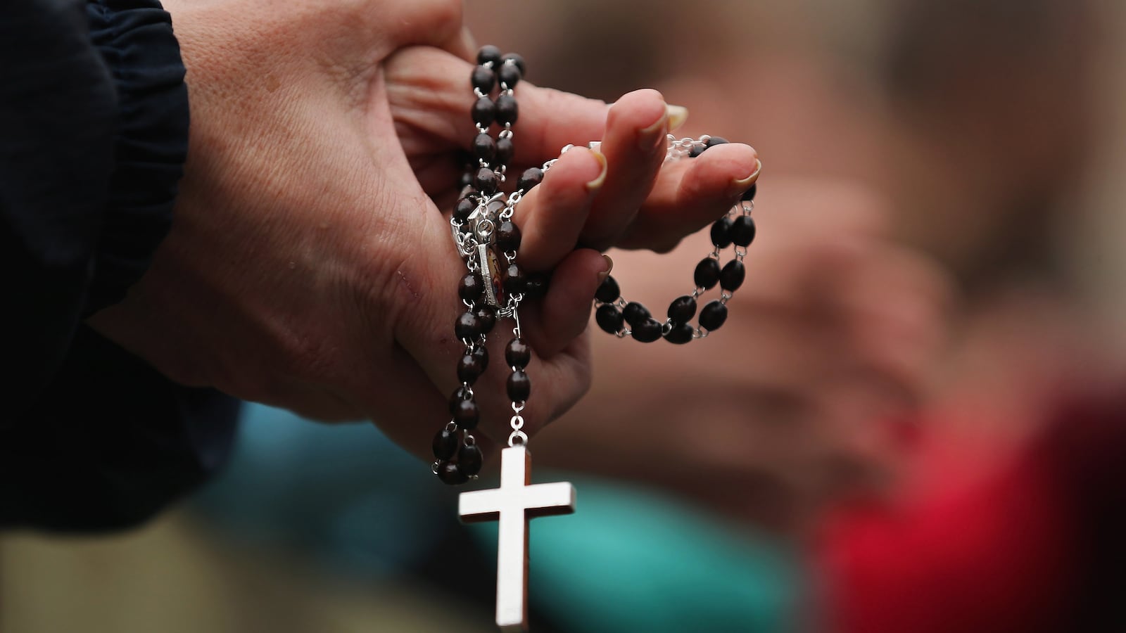 A woman holds rosary beads while she prays and waits for smoke to emanate from the chimney on the roof of the Sistine Chapel.