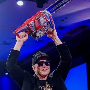 Elon Musk holds a chainsaw, wearing black sunglasses and a black hat