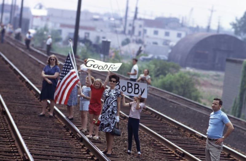People standing on train track holding signs saying "Goodbye" and "Bobby." It is the 1960s