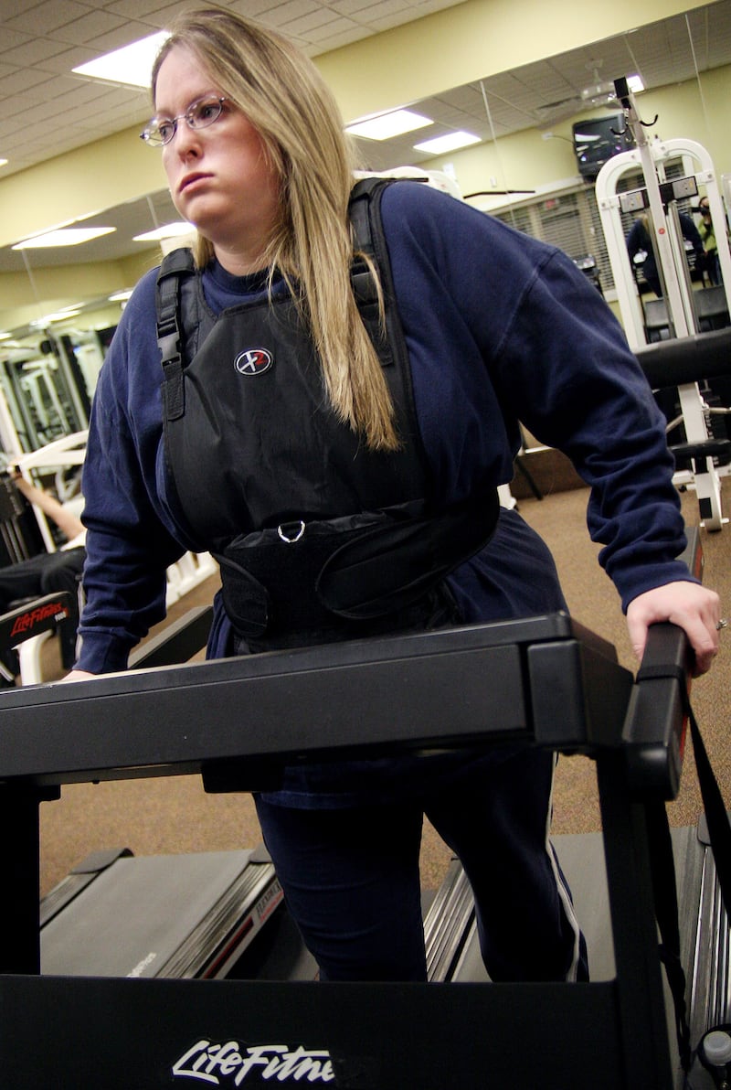 A Woman using a weighted vest while on a treadmill.