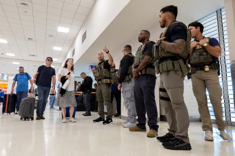 A United States Immigration and Customs Enforcement (ICE) agent assists a traveler as other agents stand inside a terminal and passengers pass by after hundreds of Immigration and Customs Enforcement agents were ordered to deploy to airports to help fill TSA staffing gaps at Luis Munoz Marin International Airport in Carolina, Puerto Rico, March 24, 2026. REUTERS/Ricardo Arduengo