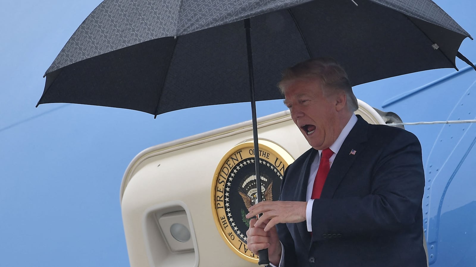 US President Donald Trump shelters from the rain under an umbrella as he disembarks from Airforce One in Los Angeles, California on March 13, 2018. (Photo by MANDEL NGAN / AFP) (Photo by MANDEL NGAN/AFP via Getty Images)