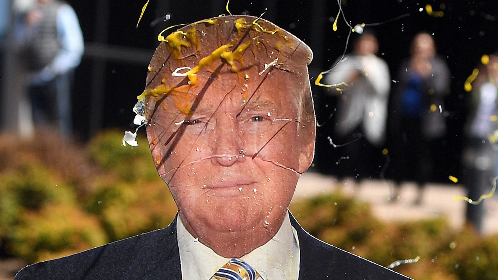 An egg is thrown at a cardboard cutout of Donald Trump.