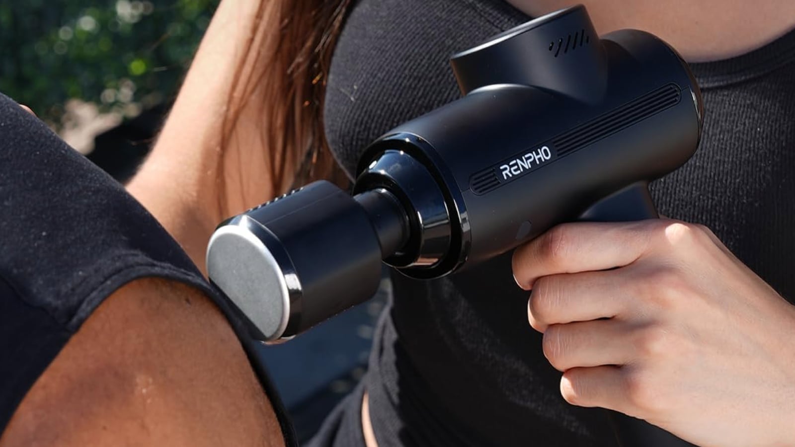 Woman using the RENPHO Thermacool 2 Massage Gun on a man's shoulder outdoors.