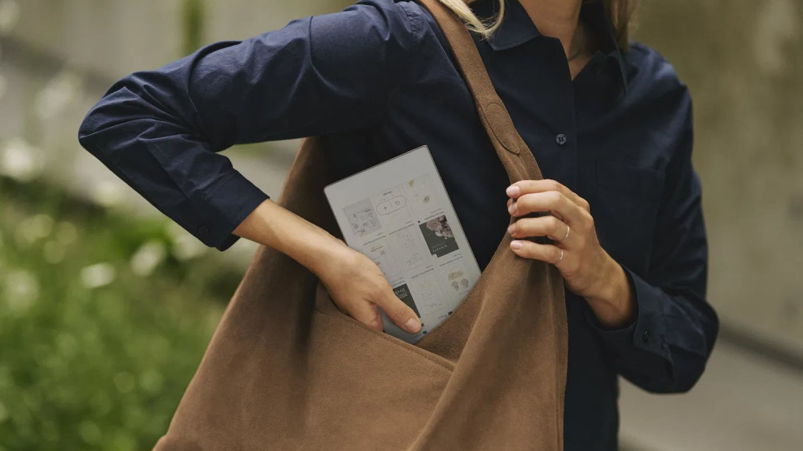 A woman wearing a blue shirt putting her reMarkable Paper Pro Move tablet into her brown shoulder bag.