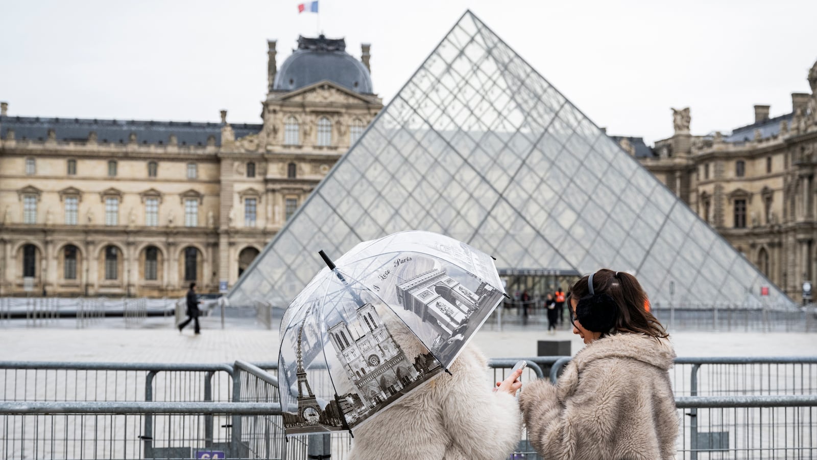 Tourists stand next to barriers blocking the plaza with the Louvre Pyramid, designed by Chinese-US architect Ieoh Ming Pei, as the Louvre Museum is closed due a strike in Paris on January 12, 2026. The Louvre museum was forced to close on January 12, 2026 after its staff, who have been on strike since mid-December in a bid to secure better working conditions, decided to continue their action, AFP learned from the museum and trade unions. (Photo by Martin LELIEVRE / AFP via Getty Images) / RESTRICTED TO EDITORIAL USE - MANDATORY MENTION OF THE ARTIST UPON PUBLICATION - TO ILLUSTRATE THE EVENT AS SPECIFIED IN THE CAPTION