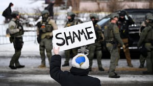 An onlooker holds a sign that reads "Shame" as members of law enforcement work the scene following a suspected shooting by an ICE agent during federal law enforcement operations on January 07, 2026 in Minneapolis, Minnesota. According to federal officials, the agent, “fearing for his life” killed a woman during a confrontation in south Minneapolis.