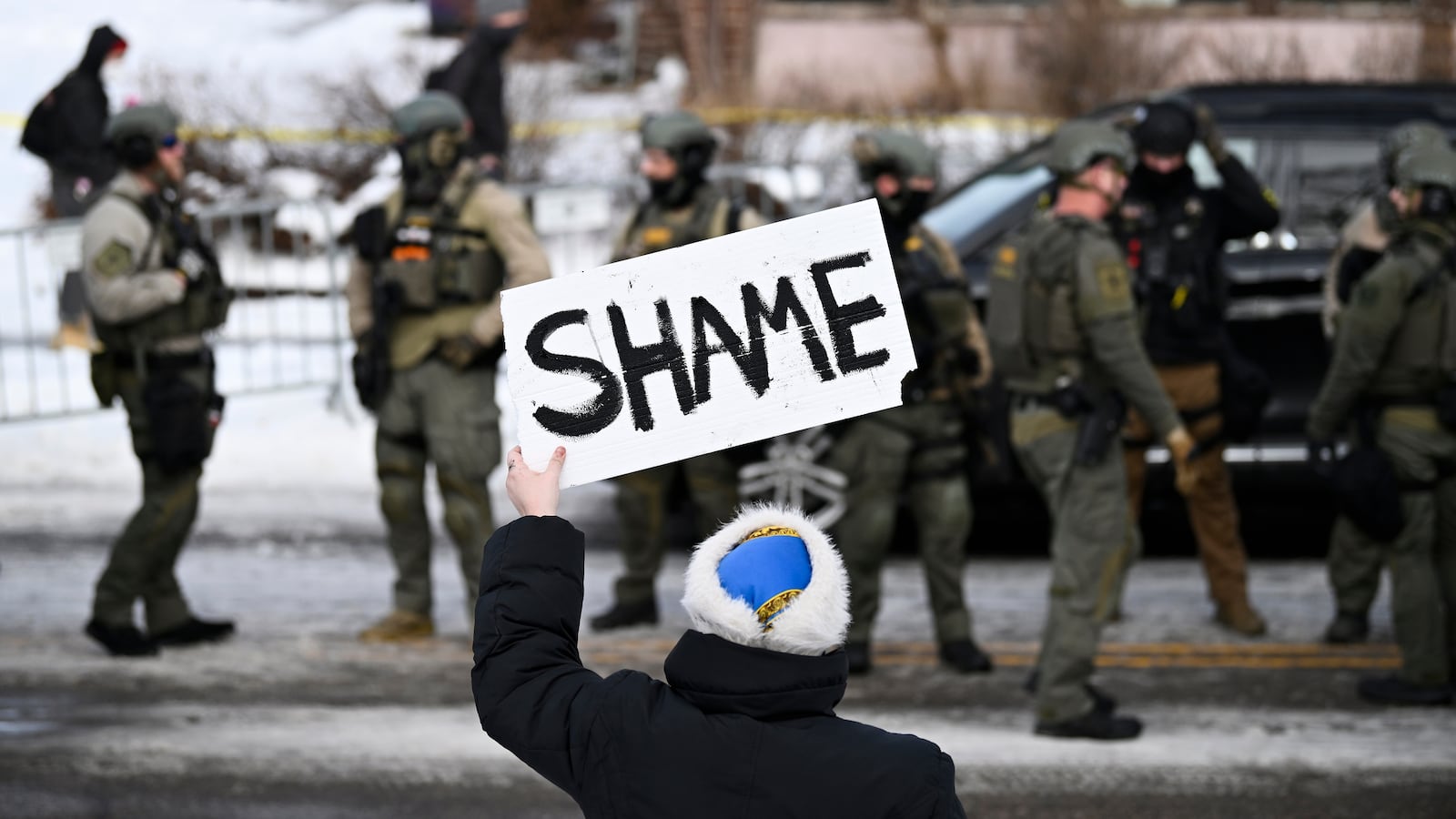 An onlooker holds a sign that reads "Shame" as members of law enforcement work the scene following a suspected shooting by an ICE agent during federal law enforcement operations on January 07, 2026 in Minneapolis, Minnesota. According to federal officials, the agent, “fearing for his life” killed a woman during a confrontation in south Minneapolis.