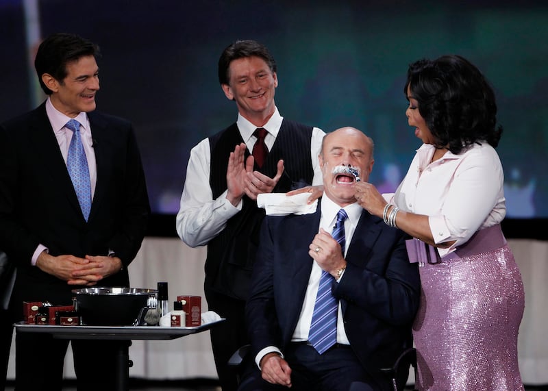 Television personality Dr. Oz (L) watches as U.S. talk show host Oprah Winfrey (R) shaves off the moustache of television personality Dr. Phil during a special show at Radio City Music Hall in celebration of O Magazine's 10th anniversary in New York City, May 7, 2010.