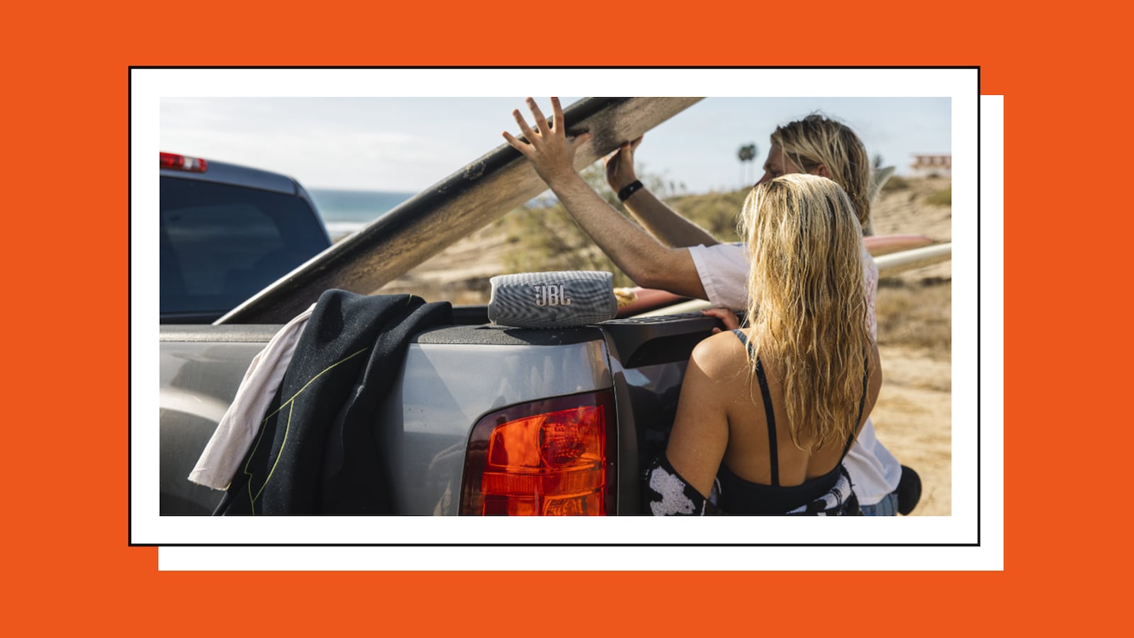 A man and woman unloading a pickup truck at a beach. There is a portable speaker on the truck with the letters JBL on it.