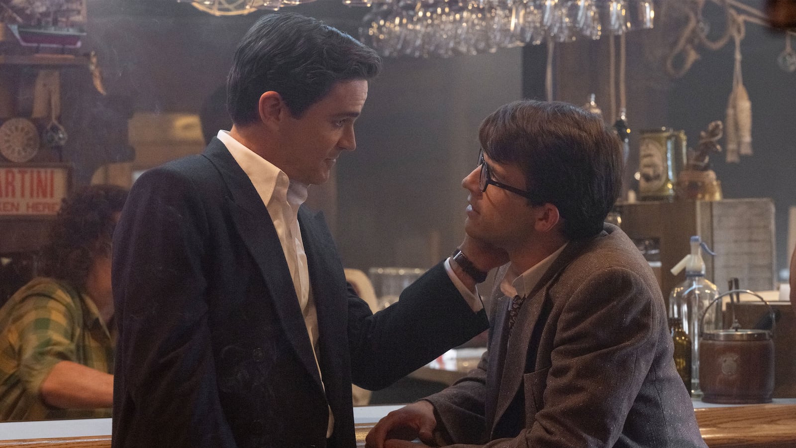 Matt Bomer touches Jonathan Bailey's face while they sit at a bar in a still from 'Fellow Travelers'