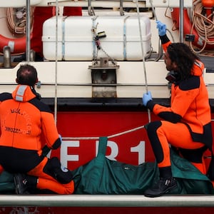 Divers board a ship with a body bag.
