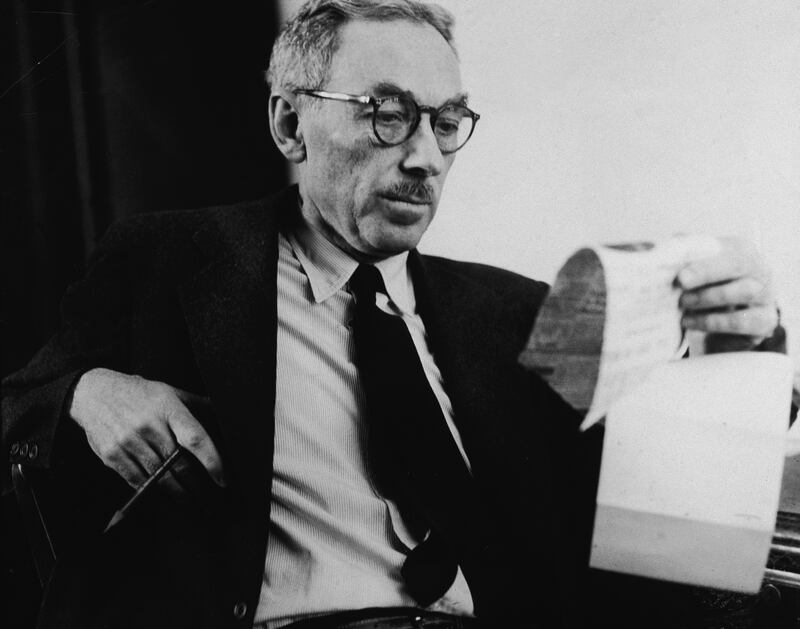 American writer E.B. White (1899 - 1985) reads a newspaper clipping in his office at the New Yorker