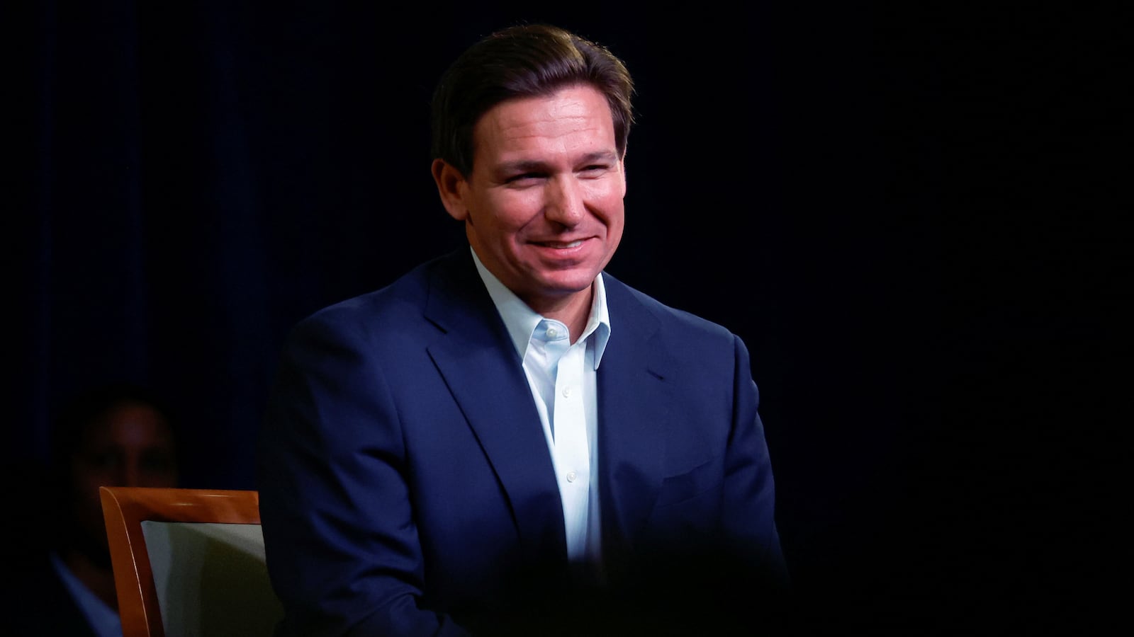 Florida Gov. Ron DeSantis smiles in a darkly lit room
