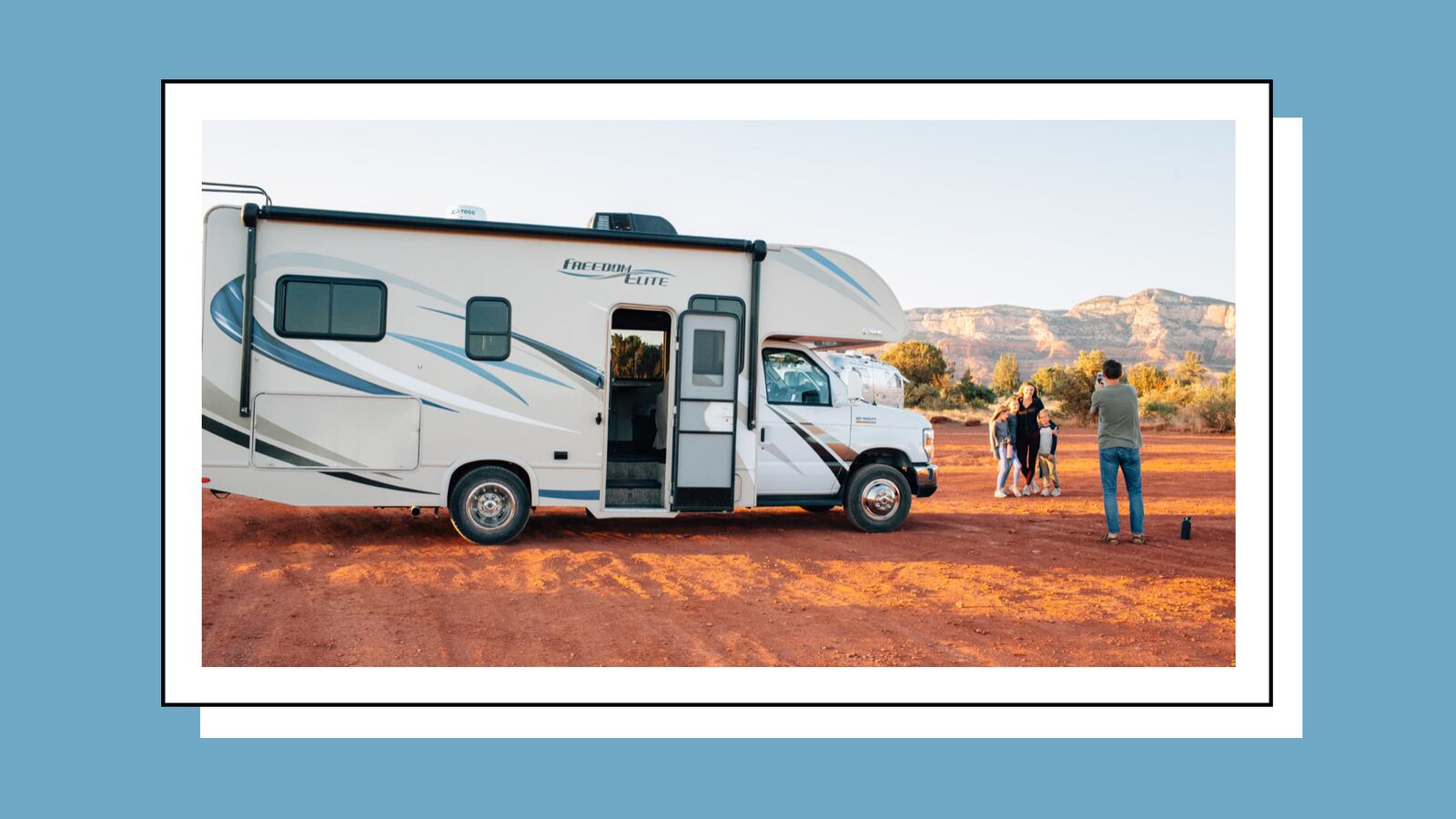 A man taking a photo of his wife and kids near an RV that's out on a desert.