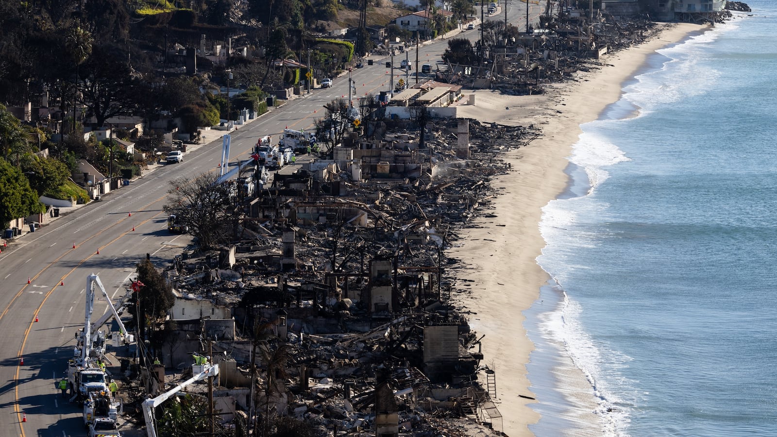 Vehicles run on the Palisades section of Pacific Coast Highway along scorched structures and trees by wildfires on January 12, 2025 in Los Angeles, California. The Palisades and Eaton fires have forced tens of thousands of residents to flee this week, leaving many wondering what may remain of their homes in Pacific Palisades, Altadena and surrounding areas.